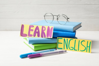 Phrase LEARN ENGLISH, books, glasses and felt tip pens on white wooden table
