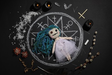 Female voodoo doll with pins surrounded by ceremonial items on black background, flat lay