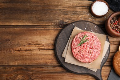 Raw hamburger patties with rosemary and spices on wooden table, flat lay. Space for text