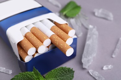 Pack of cigarettes, menthol crystals and mint leaves on grey background, closeup