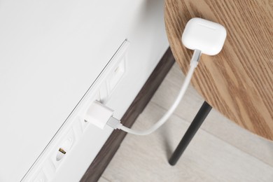 Modern wireless earphones charging from electric socket indoors, above view