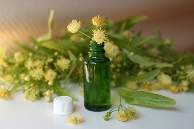 Photo of Bottle of essential oil with linden blossoms on white table