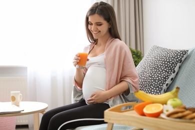 Young pregnant woman holding glass with juice at home