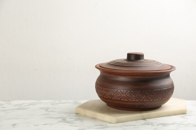 Brown clay pot on white marble table, space for text. Handmade utensil