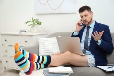 Businessman in shirt, underwear and funny socks talking on phone during video call at home