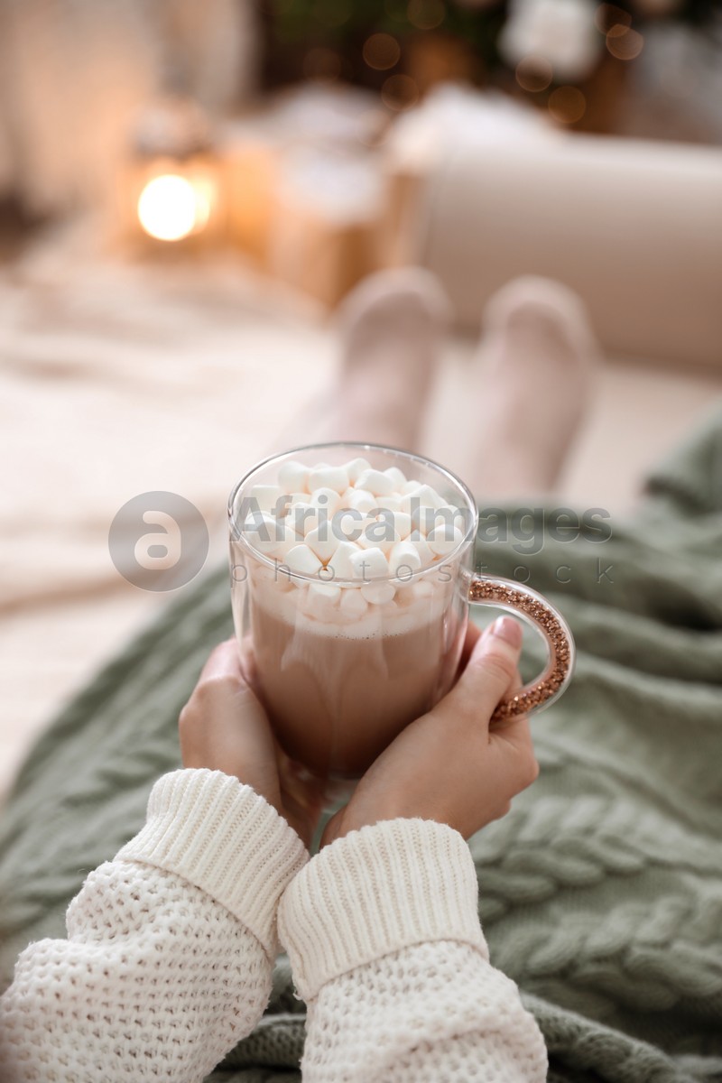 Woman with delicious hot drink wrapped in plaid on sofa at home, closeup