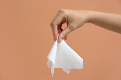 Woman holding paper tissue on light brown background, closeup