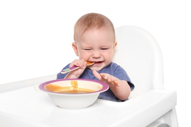 Adorable little child having breakfast in highchair against white background. Healthy baby food