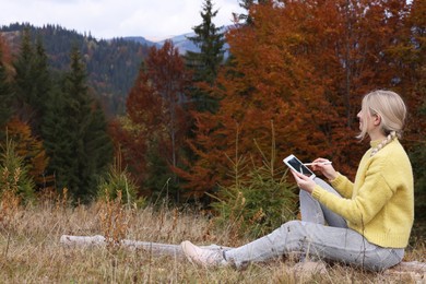 Young woman drawing with graphic tablet in mountains on autumn day