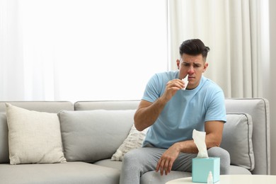 Ill man using nasal spray on sofa at home