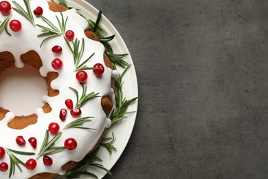 Traditional Christmas cake decorated with glaze, pomegranate seeds, cranberries and rosemary on grey textured table, top view. Space for text