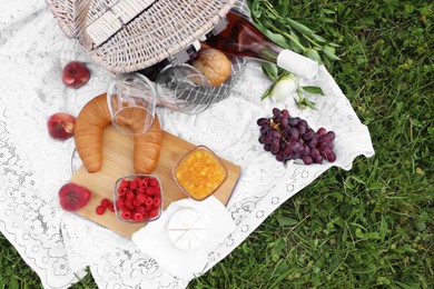 Picnic blanket with tasty food, flowers and cider on grass outdoors, flat lay