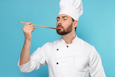 Photo of Mature male chef with spoon tasting dish on light blue background