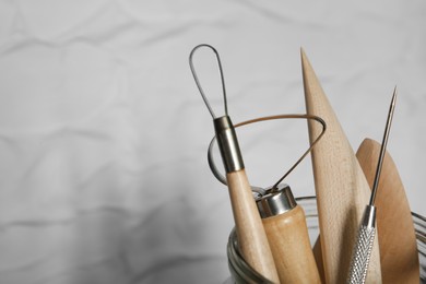 Set of clay modeling tools in glass jar near white wall, closeup. Space for text