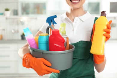 Woman with basin of detergents and bottle in kitchen, closeup. Cleaning service