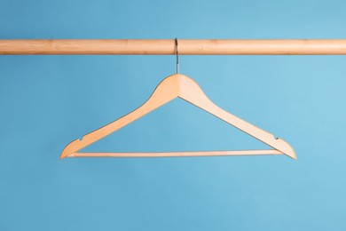 Empty clothes hanger on wooden rail against light blue background