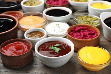 Many bowls with different sauces and herbs on wooden table