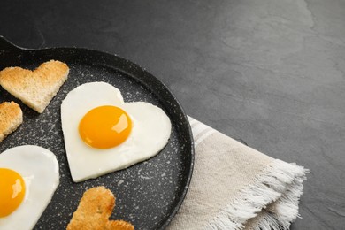 Heart shaped fried eggs and toasts in frying pan on grey table, closeup. Space for text