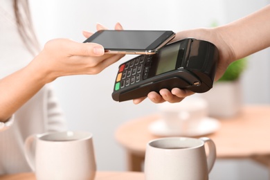 Woman using terminal for contactless payment with smartphone in cafe