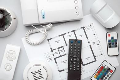 Remote controls, intercom, building plan, smoke and movement detectors on white background, flat lay. Home security system