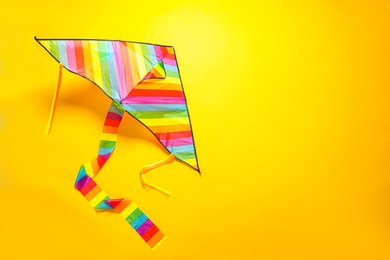 Bright rainbow kite on yellow background, top view. Space for text