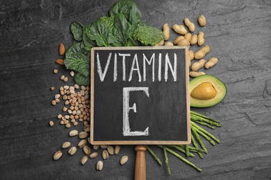 Small chalkboard with phrase Vitamin E and different products on dark background, flat lay