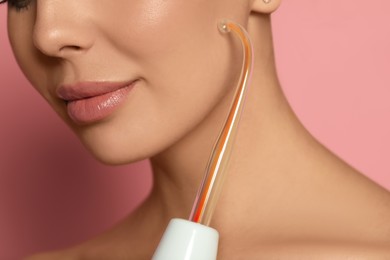 Photo of Woman using high frequency darsonval device on pink background, closeup