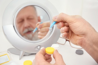 Senior man taking contact lens from container in front of mirror