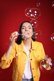 Photo of Young woman blowing soap bubbles on red background