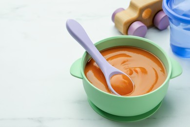 Bowl and spoon with tasty pureed baby food on white table, space for text