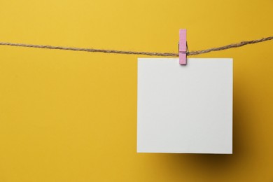 Wooden clothespin with blank notepaper on twine against yellow background. Space for text