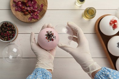 Woman in gloves with self made bath bomb at white table, top view