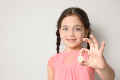 Little girl with vitamin pill against light background, focus on hand. Space for text