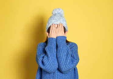 Photo of Young woman wearing warm sweater and hat on yellow background. Winter season