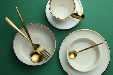 Photo of Stylish empty dishware and golden cutlery on green background, flat lay