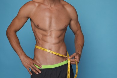 Shirtless man with slim body and measuring tape around his waist on light blue background, closeup