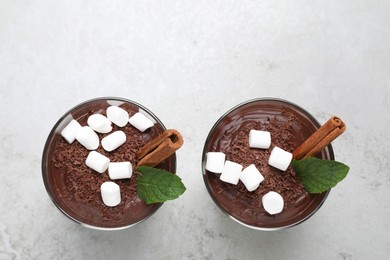 Photo of Cups of delicious hot chocolate with marshmallows, cinnamon stick and mint on light grey table, flat lay