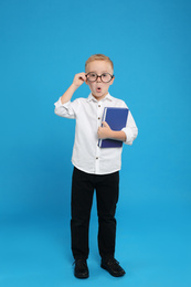 Full length portrait of cute little boy with book on light blue background