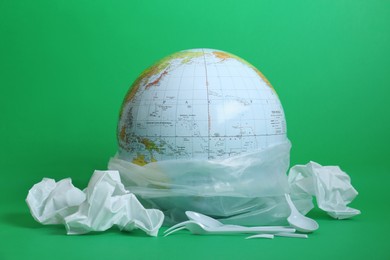 Photo of Globe in plastic bag and garbage on green background. Environmental conservation