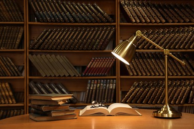 Lamp, books and glasses on wooden table in library