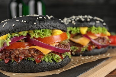 Photo of Tasty unusual black burgers on board, closeup. Space for text