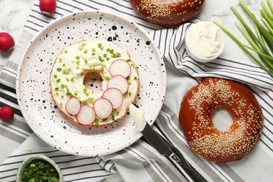 Delicious bagel with cream cheese, green onion and radish on table, flat lay