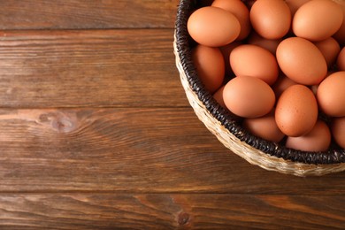 Photo of Raw chicken eggs in wicker basket on wooden table, top view. Space for text