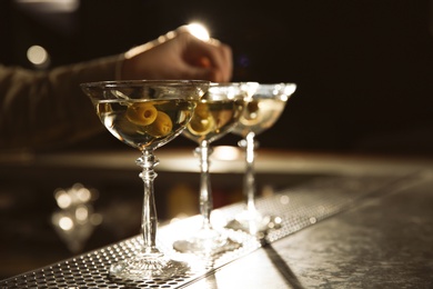 Barman adding olives to martini cocktail on counter, closeup. Space for text