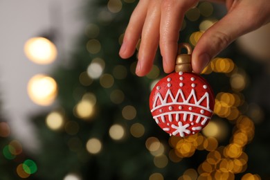 Woman holding Christmas macaron against blurred festive lights, closeup. Space for text