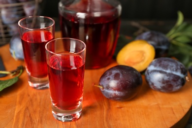 Delicious plum liquor and ripe fruits on wooden board. Homemade strong alcoholic beverage