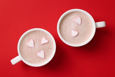 Photo of Cups of aromatic coffee with heart shaped marshmallows on red background, flat lay