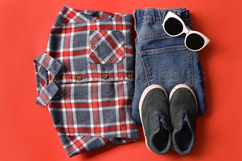 Stylish child clothes, shoes and sunglasses on red background, flat lay