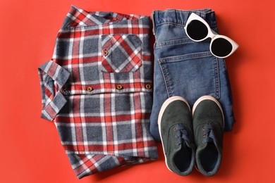 Stylish child clothes, shoes and sunglasses on red background, flat lay