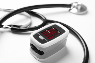 Photo of Modern fingertip pulse oximeter and stethoscope on white background, closeup